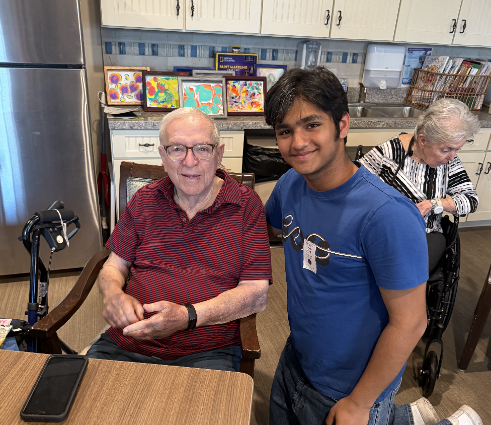 Ishaan smiles with a resident at Arbor Terrace after helping him navigate his smartphone.